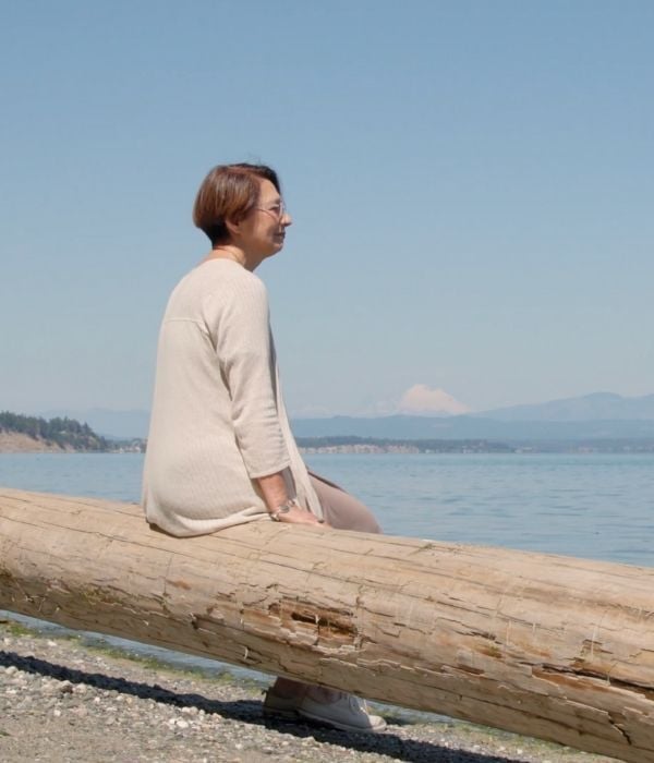 Donna watson sits on a log on the beach 